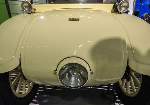 Close front view of a cream rounded bonnet with one large headlamp set low between two wings. Opens a larger view