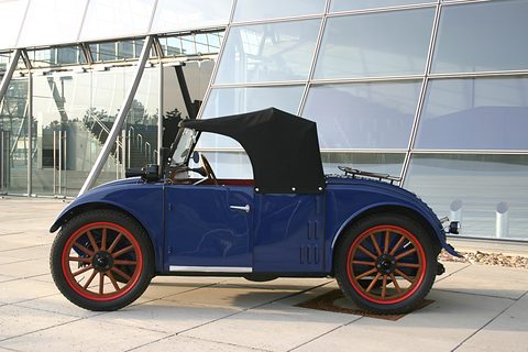 Side view of a dark blue two-seater with a black hood, red wheels and slotted vents behind the door. Opens a larger view