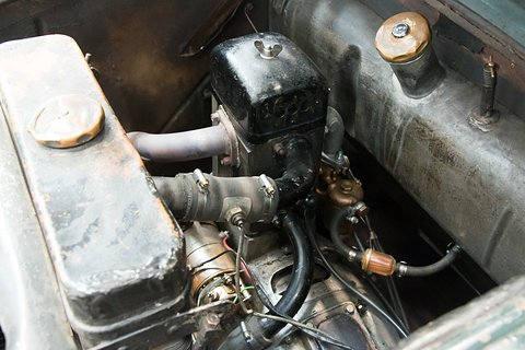 Close view of a worn single-cylinder engine with a black cooling-fan housing, pipes and a fuel filter. Opens a larger view