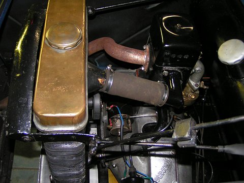 A single-cylinder engine with a black fan housing, exhaust pipe and brass-topped tank in a small rear bay. Opens a larger view