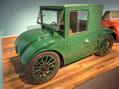 A green saloon with an open windscreen, rounded wings and wooden wheels on a wooden floor.