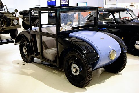 A small saloon with a black cab and pale blue bonnet, a single headlamp and black wheels on a white floor. Opens a larger view