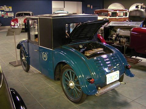 Rear three-quarter view of a blue saloon with a black cab, its louvred rear lid raised over the engine. Opens a larger view