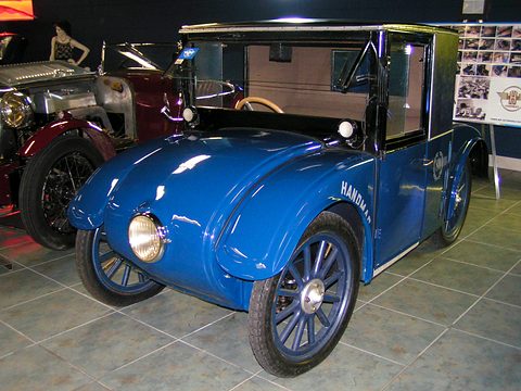 A blue saloon with a single headlamp, Hanomag lettering on its flank and blue wire wheels on a tiled floor. Opens a larger view
