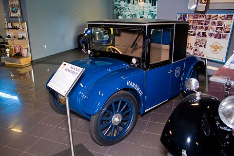 A blue saloon with Hanomag lettering on its flank and a black cab, a museum sign beside it. Opens a larger view