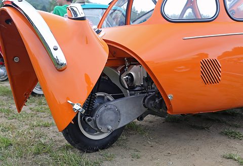 Orange bodywork with its rear panel swung open, exposing a small wheel, shock absorber and enclosed chain case. Opens a larger view