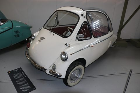 White bubble car with whitewall tyres behind a low cable, a museum caption board on the floor. Opens a larger view