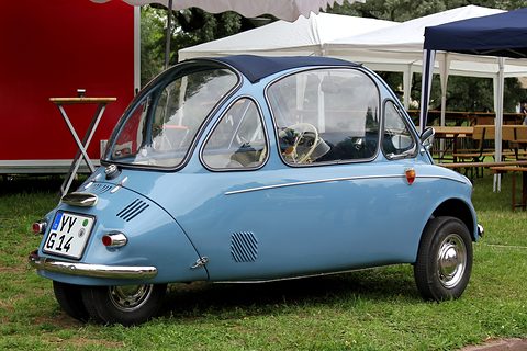 Pale blue bubble car from behind on grass, louvred tail and number plate, marquees behind.