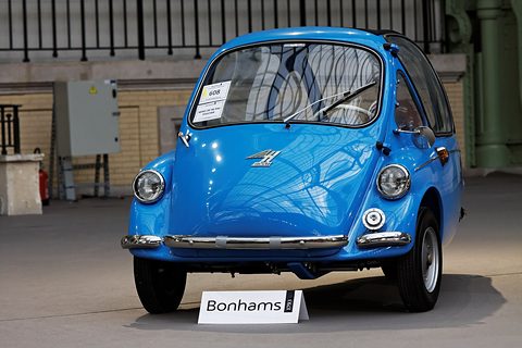 Blue bubble car facing the camera, lot card on the windscreen and a sale sign on the floor before it. Opens a larger view