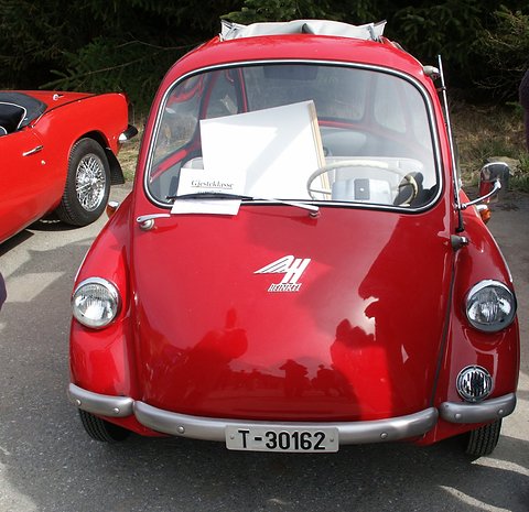 Red egg-shaped bubble car facing the camera, winged badge on its nose and a paper notice on the windscreen. Opens a larger view
