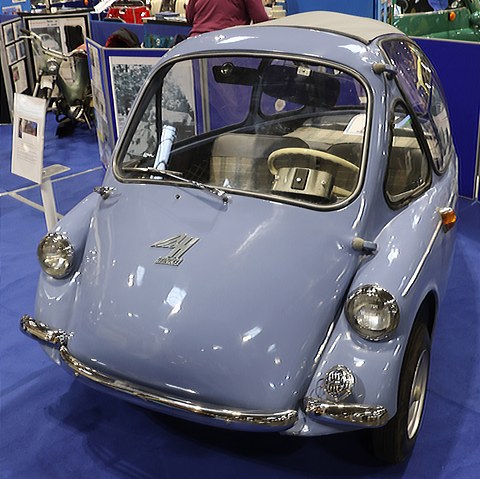 Lilac bubble car facing the camera on a blue carpet, its cream seat visible through the windscreen. Opens a larger view