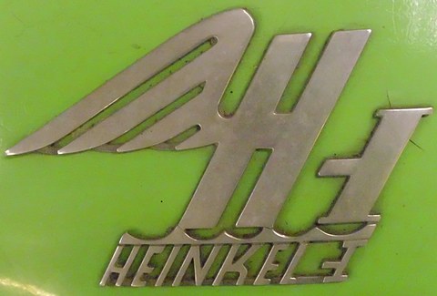 Chrome winged H emblem with HEINKEL-I lettering beneath, mounted on bright green paintwork. Opens a larger view