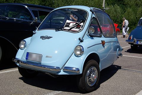 Pale blue bubble car parked on tarmac among other cars, seen from the front left