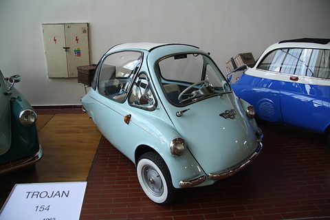 Pale blue bubble car with a picnic basket on a brick floor, a placard reading Trojan 154. Opens a larger view