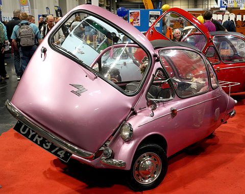 Pink bubble car with its front door raised on a red carpet, registration UYR 374, crowd behind. Opens a larger view
