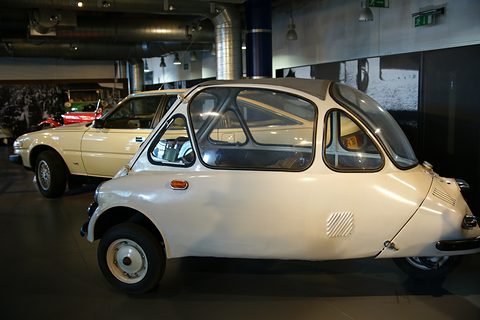 Cream bubble car in side view on a dark floor, its domed glasshouse and short tail clear. Opens a larger view