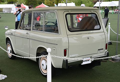 Rear of a cream small estate van with whitewall tyres on turf behind white posts and chains. Opens a larger view