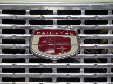 Close view of a shield-shaped red and chrome badge on a chrome slatted grille. Opens a larger view