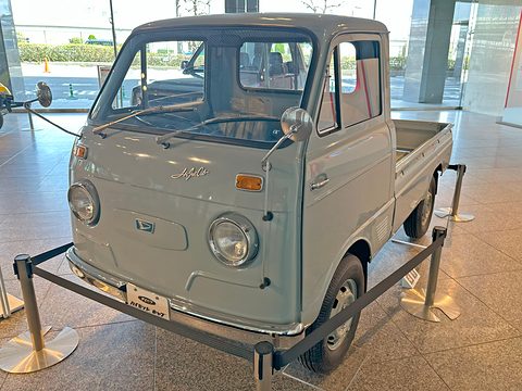 Pale blue small cab-over pick-up inside a low barrier on a speckled stone floor. Opens a larger view