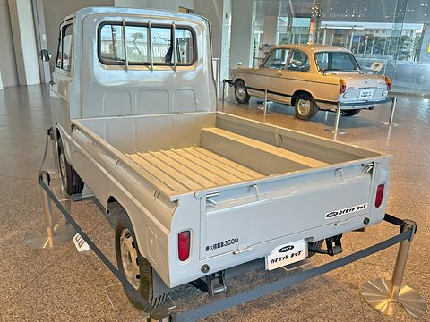 Rear of a pale blue small pick-up with a wooden-floored dropside bed inside a low barrier. Opens a larger view