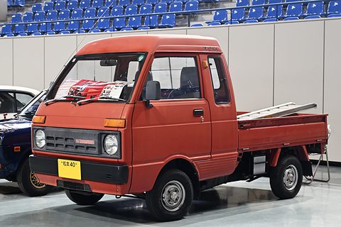 Red small cab-over pick-up with a longer cab and a brochure on the windscreen in a hall. Opens a larger view