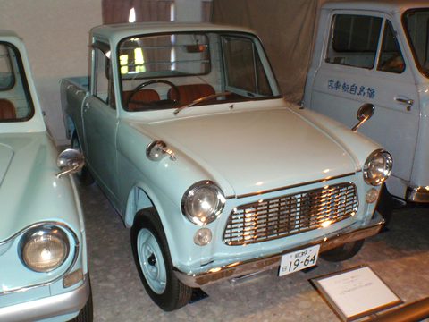 Pale blue small bonneted pick-up with a chrome grille and red seats among other small vehicles. Opens a larger view