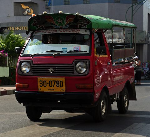 Red small cab-over truck with a decorated canopy over its bed on a town street. Opens a larger view
