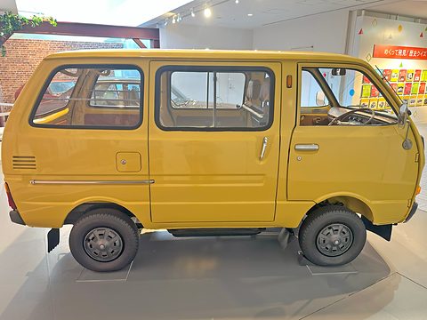 Side view of a yellow small van with sliding windows, a wall of brochures behind.