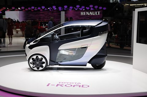 Side view of a white and navy narrow three-wheeler on a white turntable lettered Toyota i-Road.