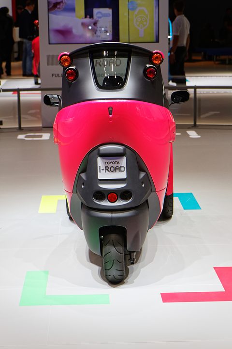 Rear of a narrow pink three-wheeler with round tail lamps, an i-Road plate and one small rear wheel. Opens a larger view