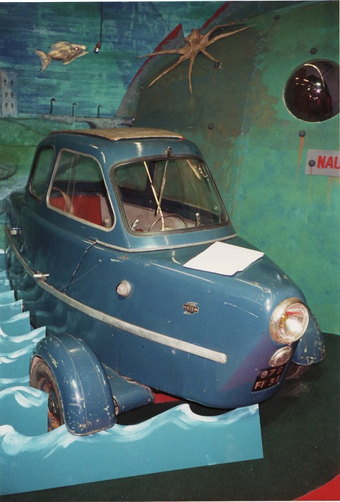 Weathered blue three-wheeler set in painted waves before a sea backdrop with a fish and a crab. Opens a larger view