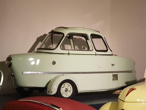 Pale green three-wheeler with a domed, many-windowed canopy and chrome side strake, seen from the side in a museum.