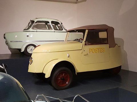 Cream small electric car lettered POSTES with a brown fabric top, a pale green canopied three-wheeler parked behind it. Opens a larger view