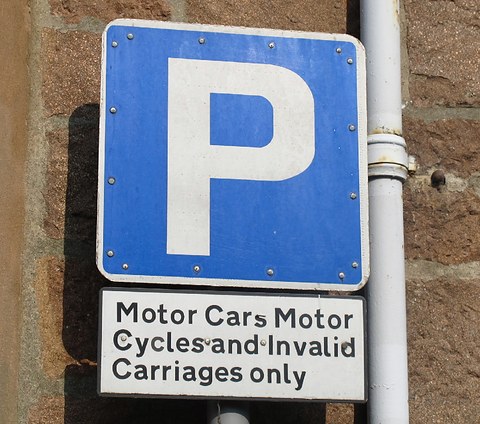 Blue P parking sign above a white plate reading Motor Cars, Motor Cycles and Invalid Carriages only, on a stone wall. Opens a larger view