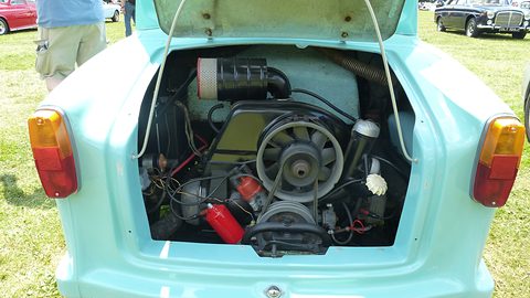 Engine bay with a cooling fan, air filter and pipes under a raised turquoise lid.