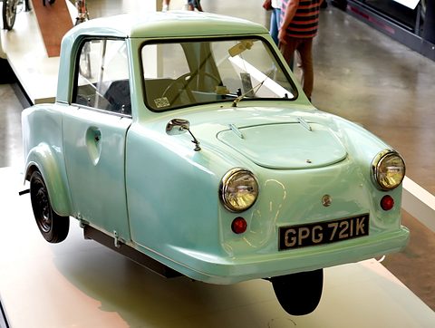 Mint-green single-seat three-wheeler on a white plinth, front wheel raised slightly.
