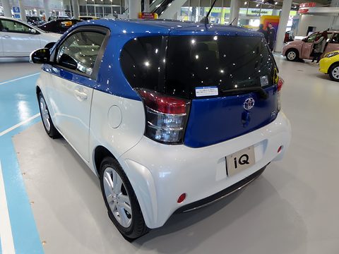 Rear of a white city car with a blue roof and tailgate on a showroom floor marked with blue lines. Opens a larger view