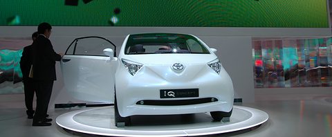 White concept hatchback on a round white turntable with its door open, two men in suits beside it. Opens a larger view