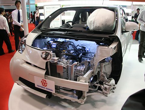 White cutaway hatchback on a red floor with its front opened to show the engine, suspension and an inflated airbag.