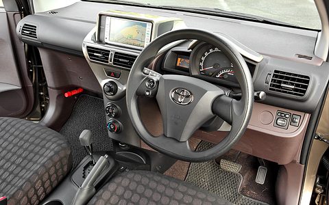 Steering wheel with a Toyota badge, a navigation screen in a silver surround and a brown and black dashboard. Opens a larger view