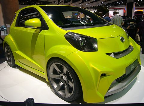 Lime-green city car with flared arches, a deep front bumper and dark wheels on a white show plinth. Opens a larger view