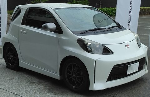 White city car with a deep body-kit bumper and black wheels parked on wet tarmac, banners behind.