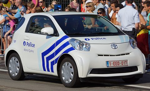 White city car with blue chevrons and Police lettering driving past a crowd behind barriers. Opens a larger view