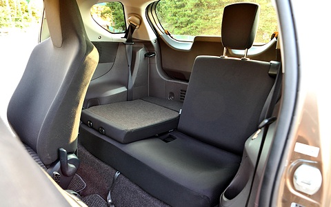 Rear compartment of a small car with one back seat folded down and a seat belt, seen through the open door. Opens a larger view