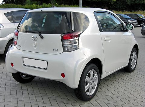 Rear of a white short city car with tall tail lamps parked on block paving. Opens a larger view