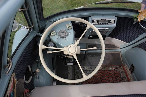 Large white steering wheel with a small speedometer behind it and a period radio in the door panel. Opens a larger view