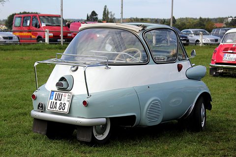Two-tone grey and white bubble car seen from behind on grass, chrome luggage rack over the rear. Opens a larger view