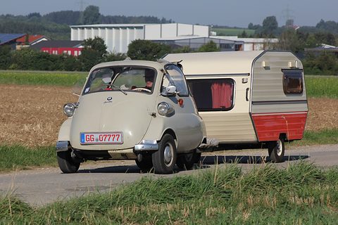 Cream bubble car pulling a little cream and red caravan along a country road. Opens a larger view