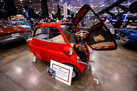 Red bubble car with its front door open on a shiny floor, a show sign leaning against it. Opens a larger view