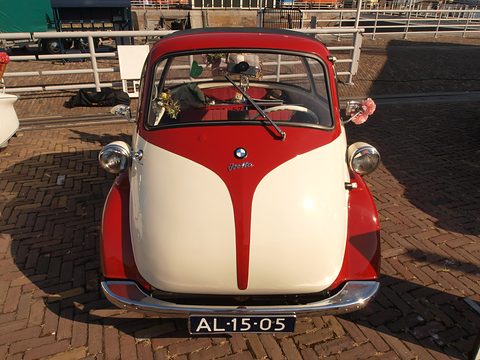 Red and cream bubble car seen from the front on brick paving, flowers on the dashboard. Opens a larger view